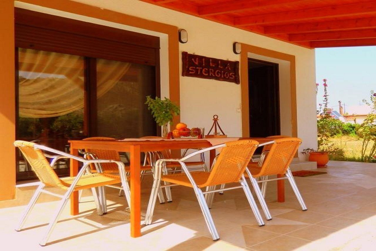 Eine überdachte Terrasse mit Tisch und Stühlen, einem Blumentopf und einem Schild mit der Aufschrift 'Villa Stergios'.