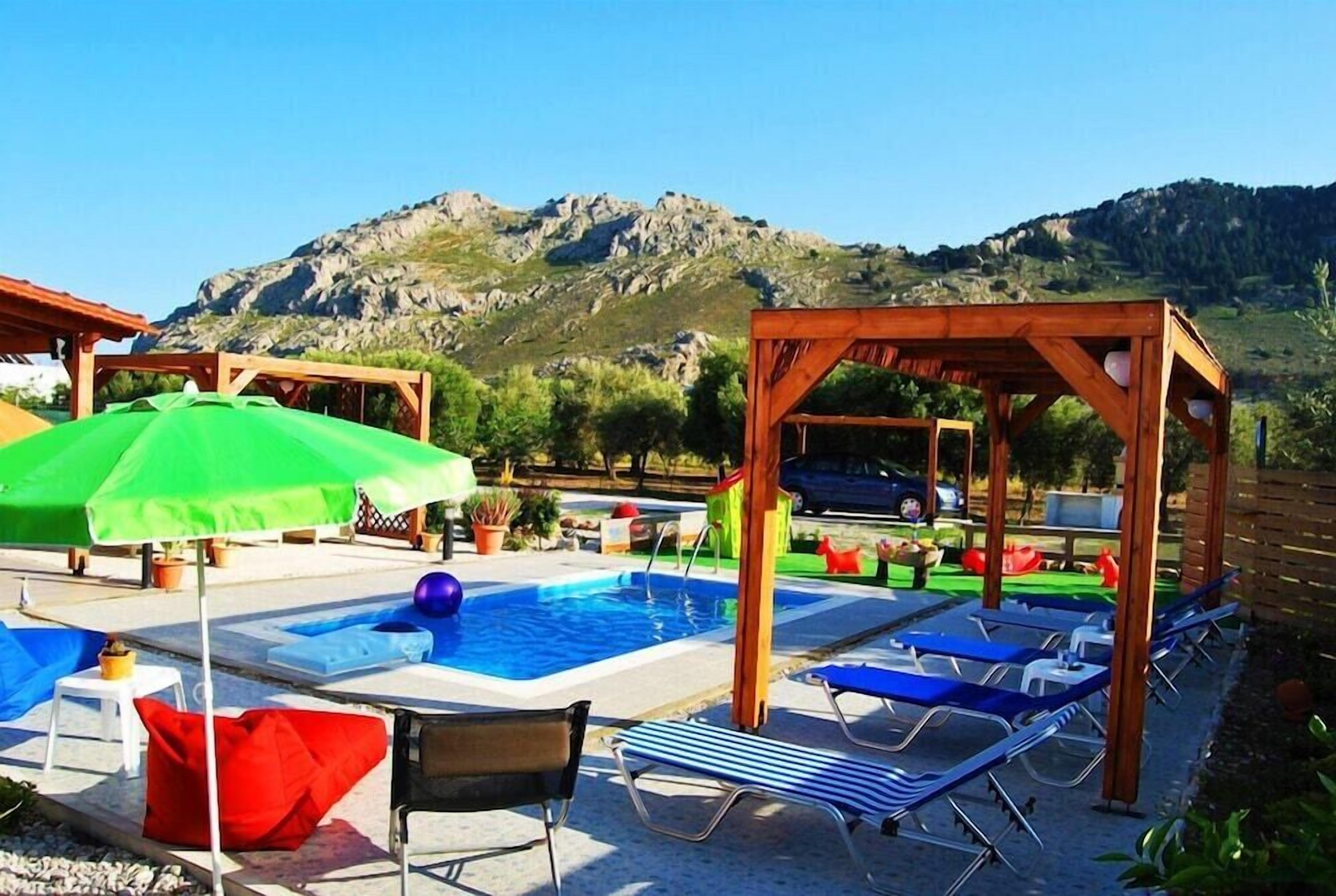 A pool area with lounge chairs, umbrellas, and a wooden pergola.