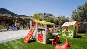 A children's play area with a slide, climbing structure, and a small house. - Stergios Villa (Rhodes)