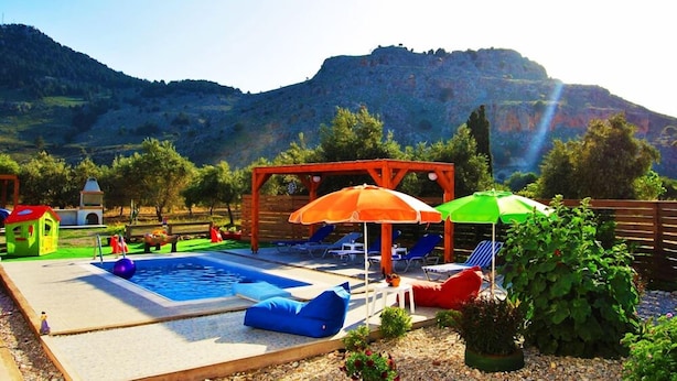 A pool area with lounge chairs and umbrellas, surrounded by greenery and a mountainous backdrop. - Stergios Villa (Rhodes)
