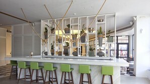 Eine moderne Küche mit einer weißen Marmorinsel, grünen Barhocker und verschiedenen topfgestellten Pflanzen auf Regalen.