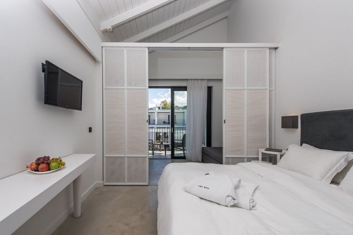 Une chambre d’hôtel moderne dotée d’un grand lit, d’un téléviseur à écran plat fixé au mur, d’une petite table de chevet et d’un balcon avec vue.