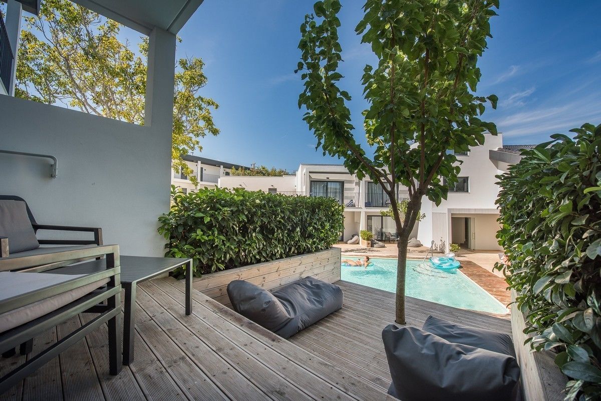 A modern outdoor patio with a pool, wooden deck, and seating area.