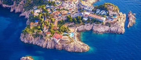 An aerial view of a coastal town with buildings, a swimming pool, and rocky terrain.