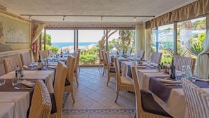 A restaurant with wicker chairs and tables, a tiled floor, and a view of the beach. - Eden Roc (Sant Feliu de Guixols)