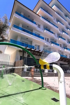 A modern building with multiple balconies, a green outdoor area with a water feature, and a clear sky. - Acuazul Hotel (Peniscola)