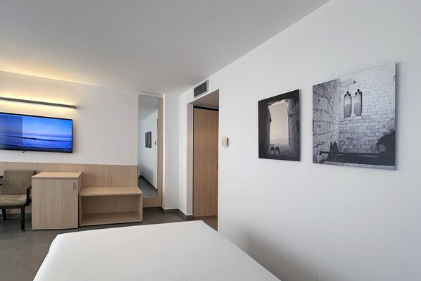 A hotel room with a bed, a desk, a chair, a flat-screen TV, and two framed pictures on the wall.