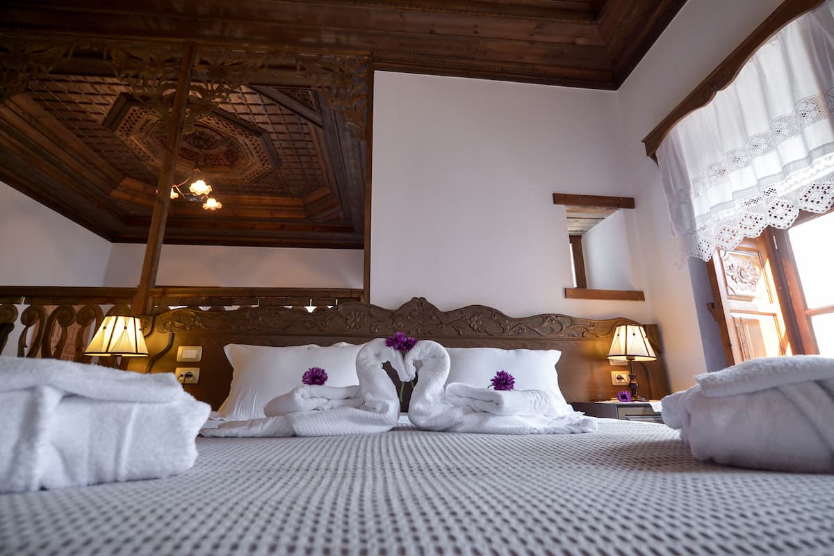A hotel room with a large bed, two bedside lamps, a wooden headboard, and a ceiling with intricate woodwork.