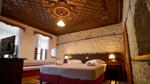 Una habitación de hotel con una cama grande, cabecero de madera, pared de piedra y techo con diseños elaborados.