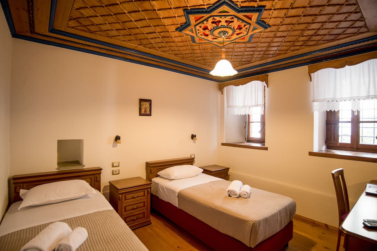 A room with two beds, a desk, and a window with lace curtains.