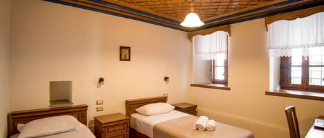A room with two beds, a desk, and a window with lace curtains.