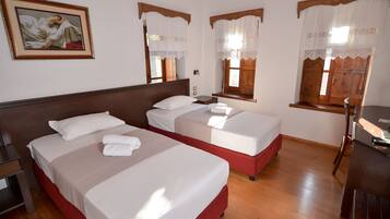 Habitación de hotel con dos camas, cabeceros de madera, un cuadro en la pared y ventanas con cortinas.