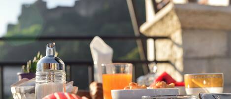 A breakfast table with a variety of food items and drinks, including a glass of orange juice, a bowl of olives, and sliced fruit.