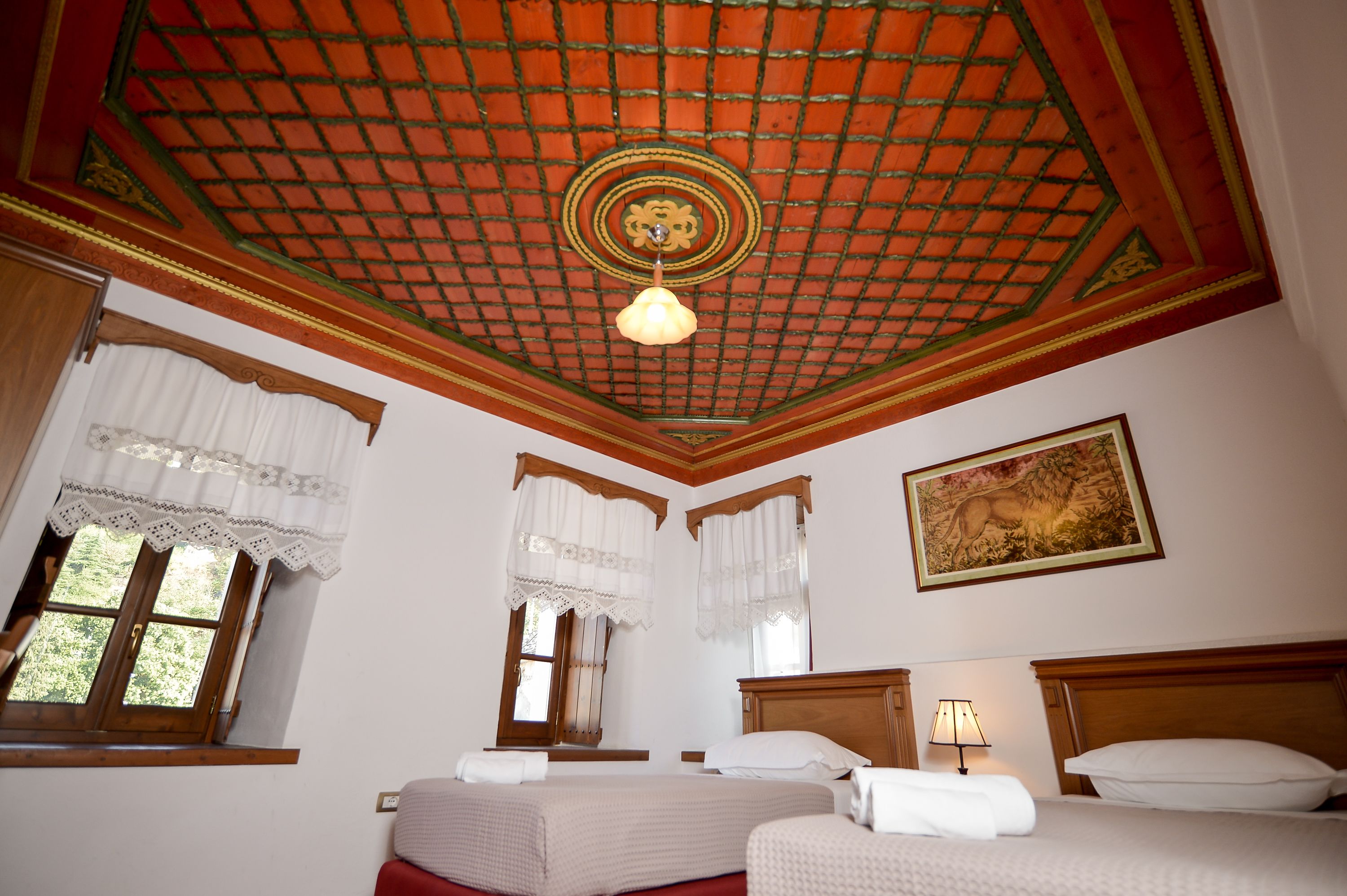 Une chambre d’hôtel avec deux lits, une tête de lit en bois, un plafond orné d’un motif en réseau et un tableau accroché au mur.