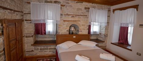A bedroom with stone walls, a wooden ceiling, a bed with white linens, and a red patterned rug.