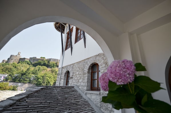 A stone building with arched windows and a view of a castle on a hill. - Hotel Kalemi 2 (Gjirokastër)