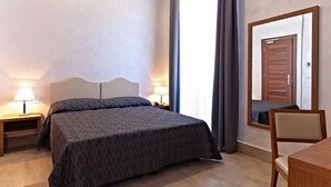 Ein Schlafzimmer mit einem großen Bett, einem Nachttisch, einem Sessel und einem Spiegel, der die Tür wiederspiegelt.