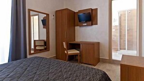 Ein Hotelzimmer mit Bett, Schreibtisch, Stuhl, Wandfernseher und einem großen Spiegel.