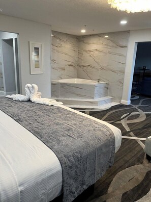 A modern hotel room with a large bed, a bathtub, and a marble wall.