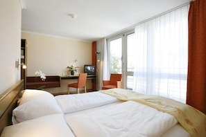 A hotel room with a bed, a desk with a chair, a television, and a window with curtains. - Ambassador (Lucerne)