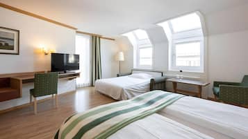 A hotel room with a bed, a desk with a TV, a chair, a lamp, and a window.