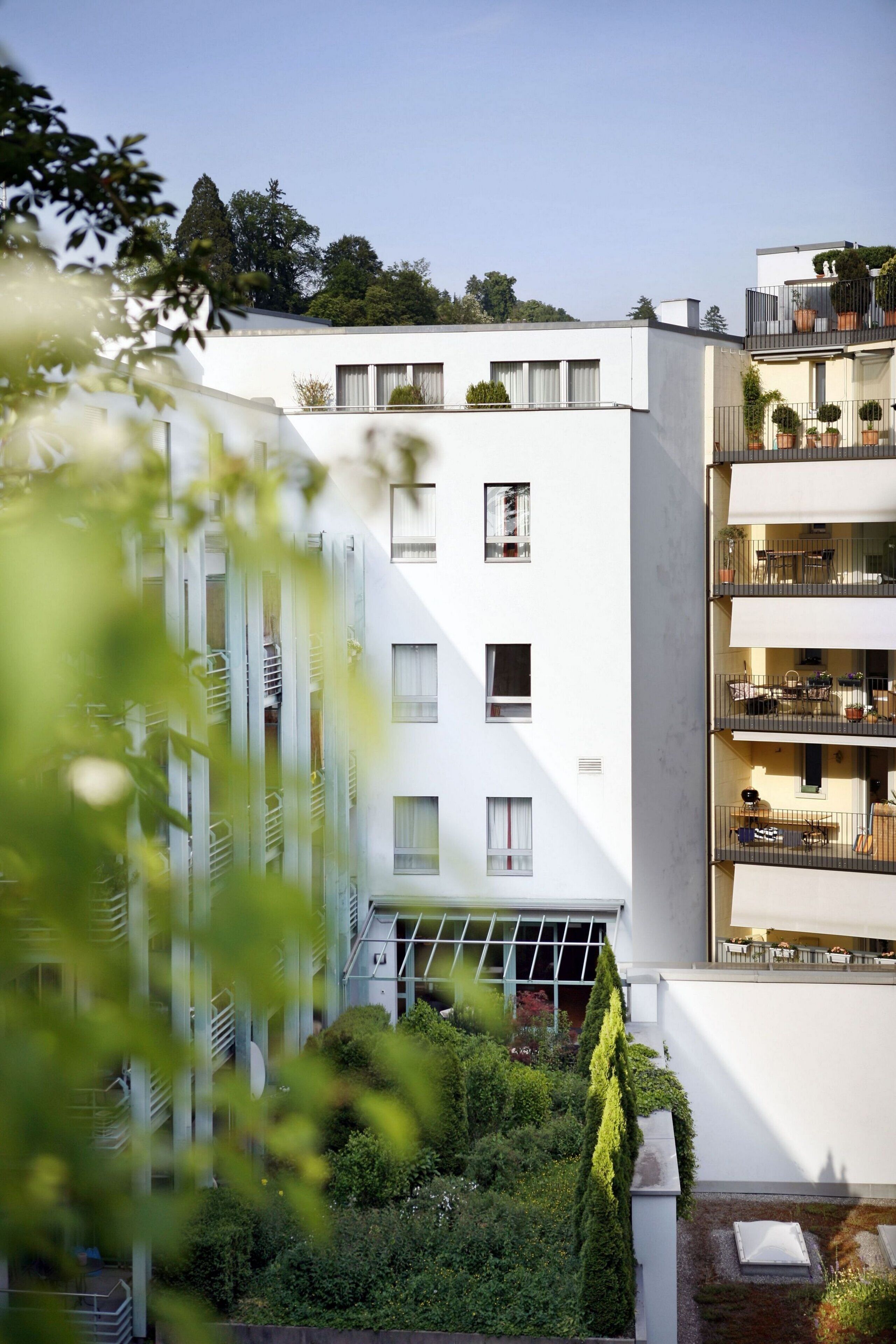 A modern multi-story residential building with balconies, large windows, and a rooftop garden.