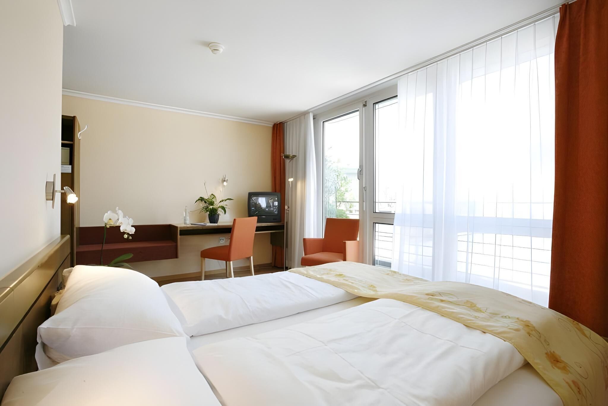 Ett hotellrum med två sängar, ett skrivbord med en tv, en stol och ett stort fönster.