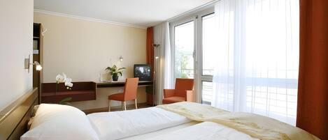 Ett hotellrum med två sängar, ett skrivbord med en tv, en stol och ett stort fönster.