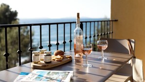 A table with a bottle of wine, two glasses, jars of jam, and bread on a balcony overlooking the sea. - La Residence du Bailli (Rayol-Canadel-sur-Mer)