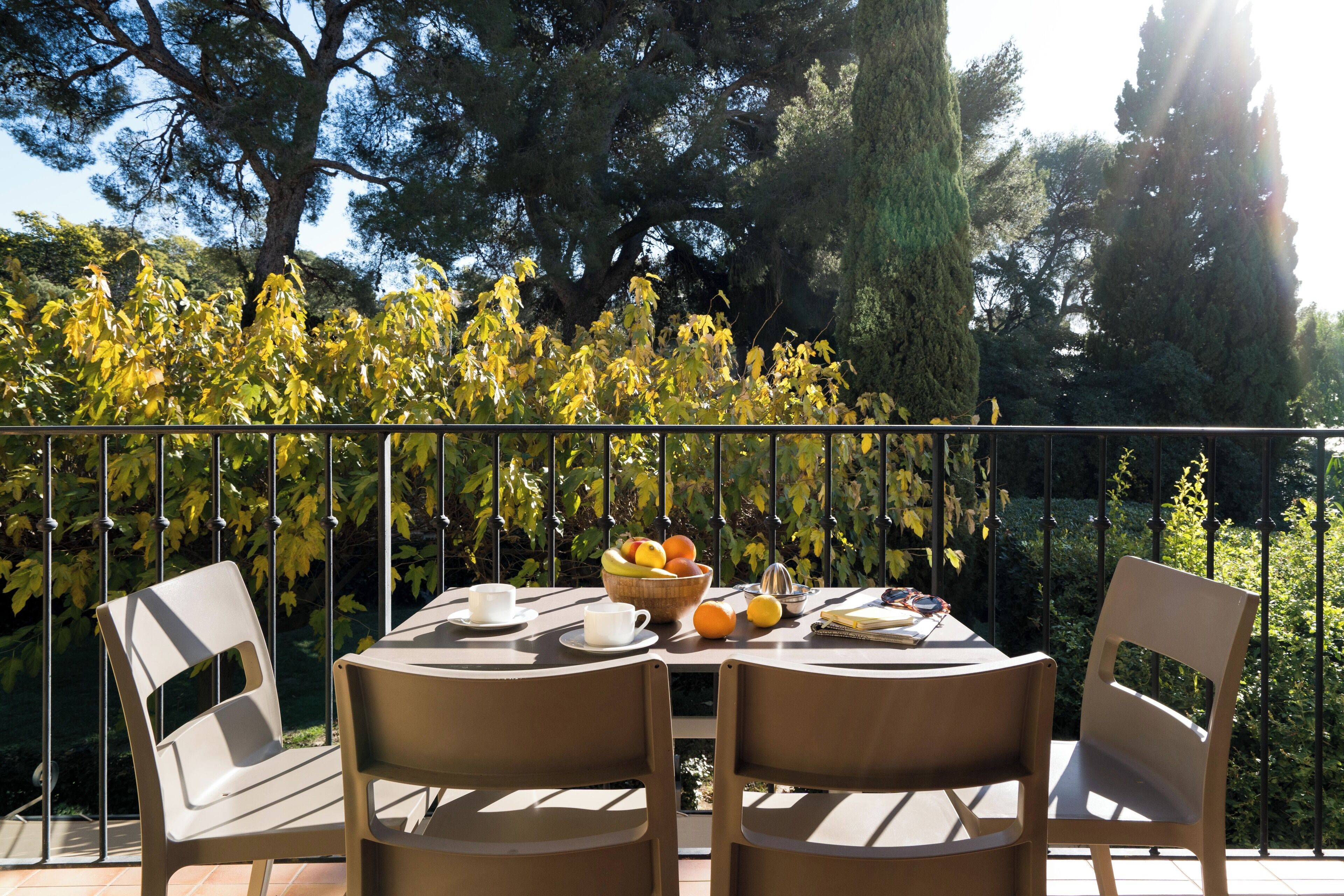 A round table with chairs, a bowl of fruit, and a book on a balcony with a metal railing.