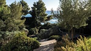 A coastal garden with a wooden deck, dense greenery, and a view of the sea. - La Residence du Bailli (Rayol-Canadel-sur-Mer)