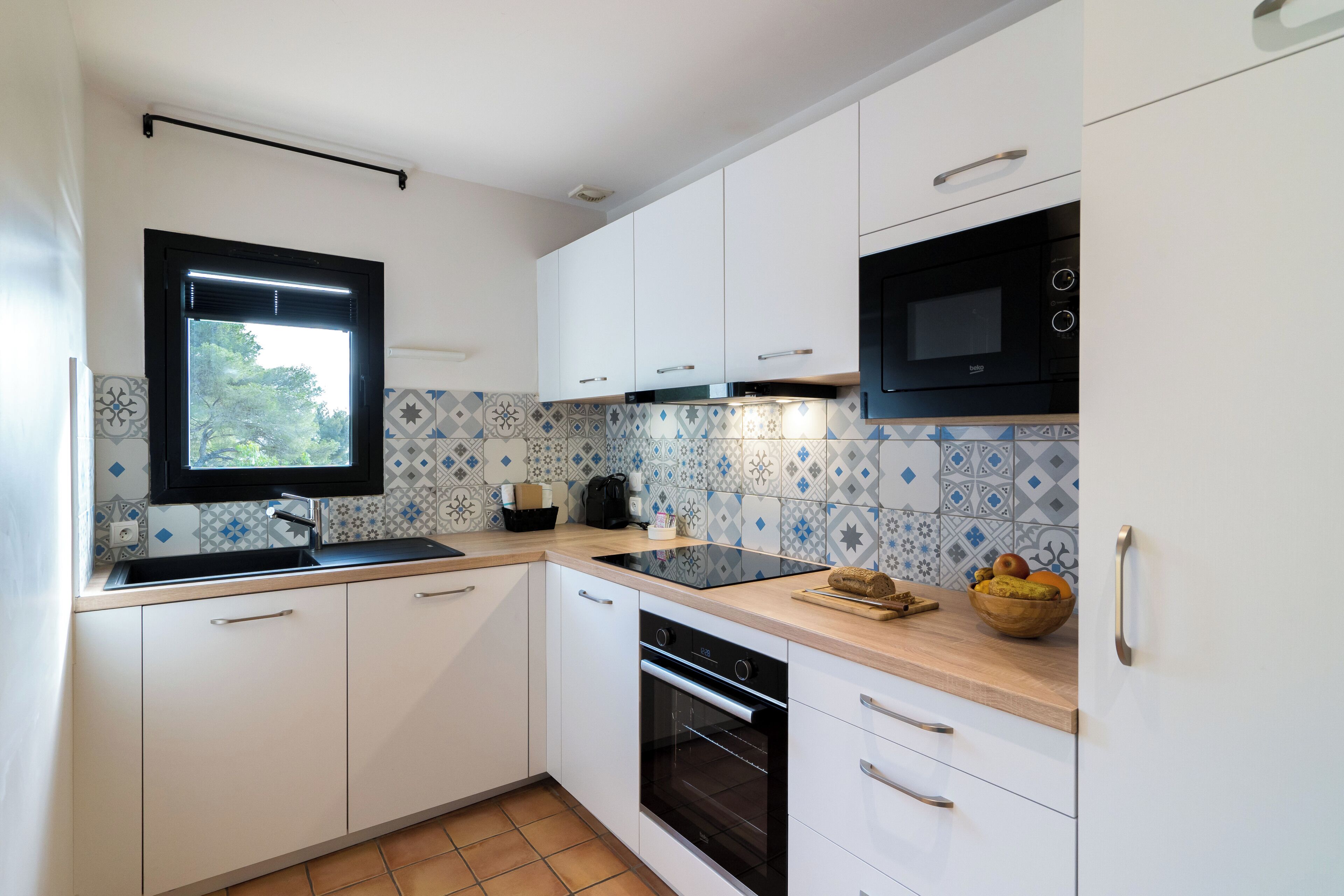 Una cocina moderna con armarios blancos, un microondas negro y un salpicadero de azulejos.
