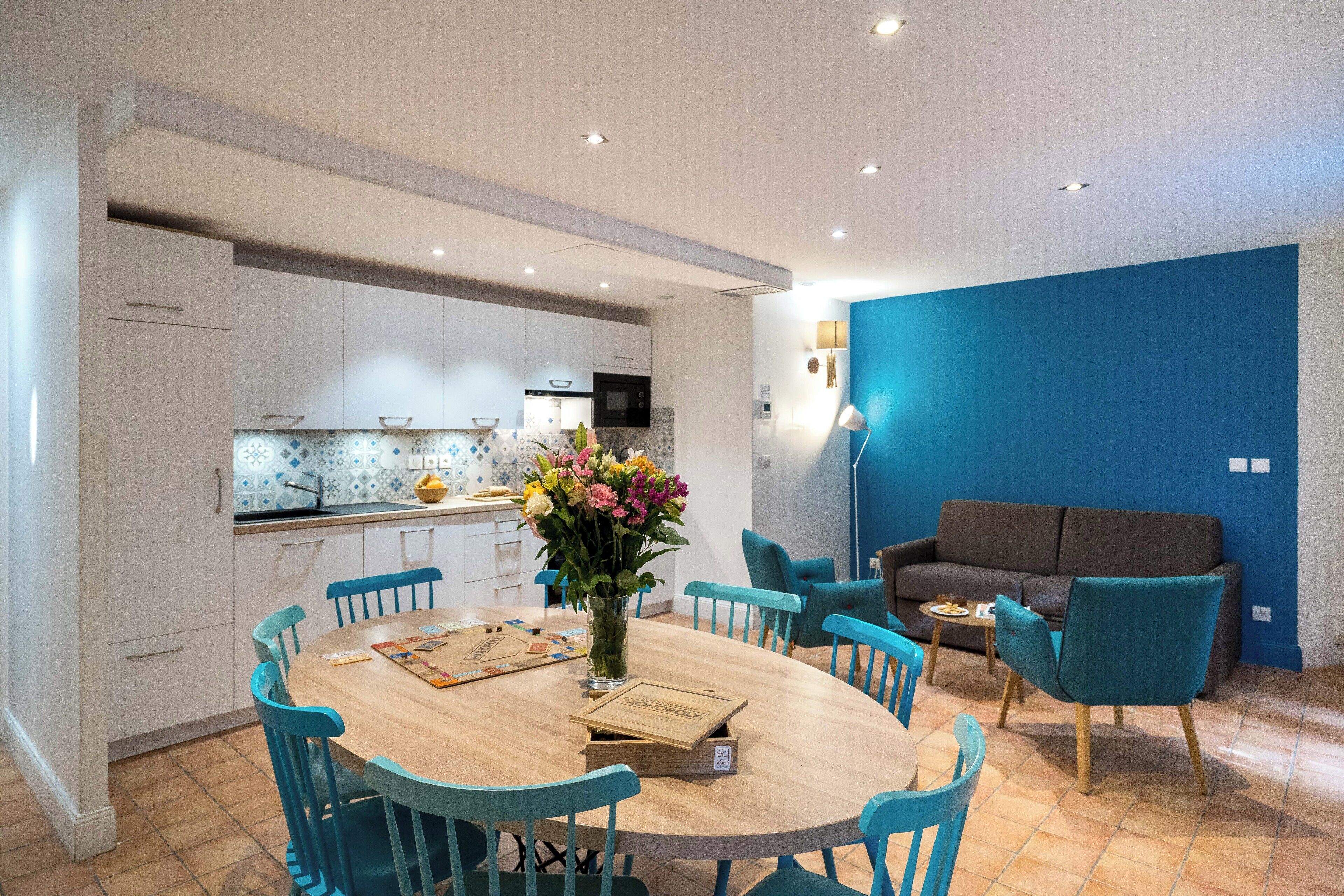 Een moderne keuken met witte kasten, een houten eettafel en blauwe stoelen.
