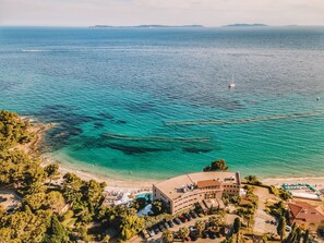 Vista aérea de un hotel costero con piscina, playa y aguas azul turquesa.