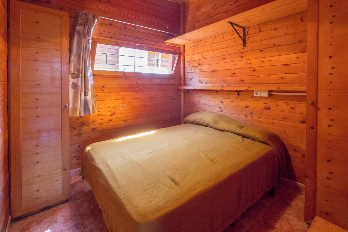 Una habitació petita i acollidora amb un llit individual, una finestra amb cortines i parets de fusta.