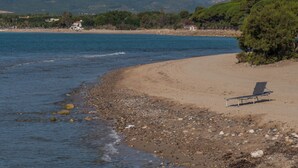 Une plage avec une chaise et un rivage rocheux, des montagnes en arrière-plan et un bâtiment avec un toit rouge.