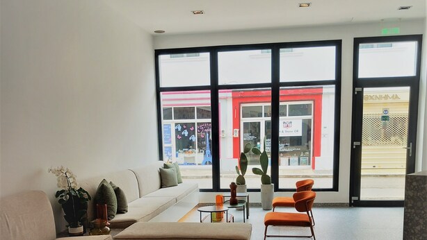 A modern living room with a sofa, a coffee table, and a chair. There is a large window with a view of a building outside. - Bianco Hotel (Leros)