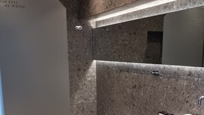 A modern bathroom with a large mirror, a white sink, and a shower area. - Bianco Hotel (Leros)