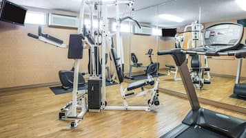 A gym with various exercise machines, a treadmill, and a mirrored wall.