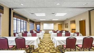 A conference room with multiple tables and chairs, a projector screen, and a patterned carpet.