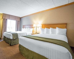 A hotel room with two beds, a wooden headboard, a nightstand with a lamp, and a window with curtains. - Quality Inn & Suites Casper Near Event Center (Casper)