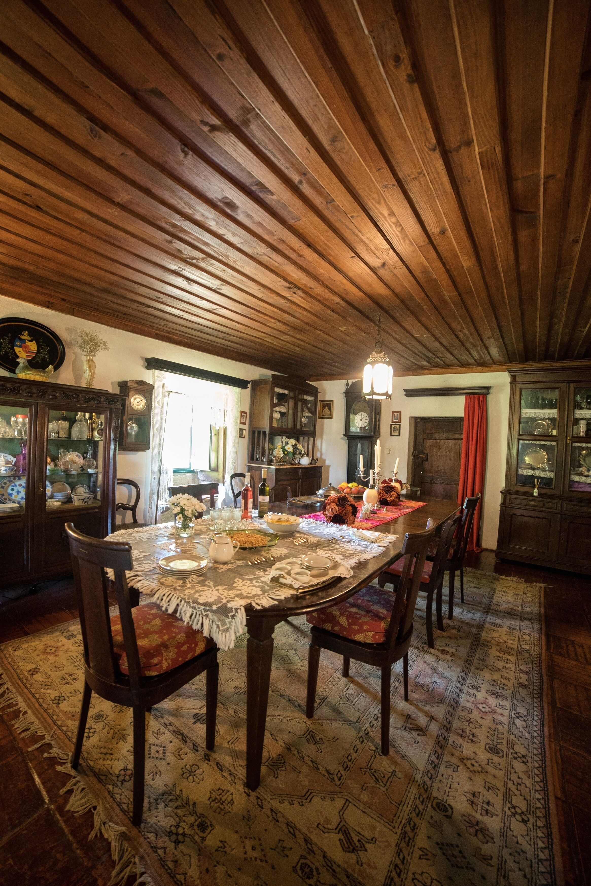 A dining room with a wooden ceiling, a large table set for four, and a patterned rug.
