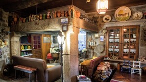 A rustic interior with a stone wall, wooden furniture, and a variety of pottery and glassware displayed on shelves and tables. - Quinta De Santa Baia (Ponte de Lima)
