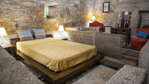 A stone-walled bedroom with a bed, two bedside tables with lamps, a chair, and a small table with decorative items. - Quinta De Santa Baia (Ponte de Lima)