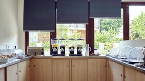 Cuina amb armaris de fusta, zona de cafè amb dispensadors i vista a la verdura a l'exterior.