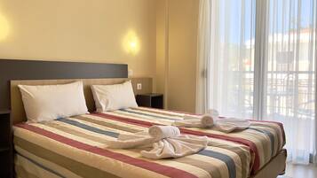 Une chambre d’hôtel avec un grand lit, deux oreillers, une couvre-lit à rayures et une fenêtre avec des rideaux légers.