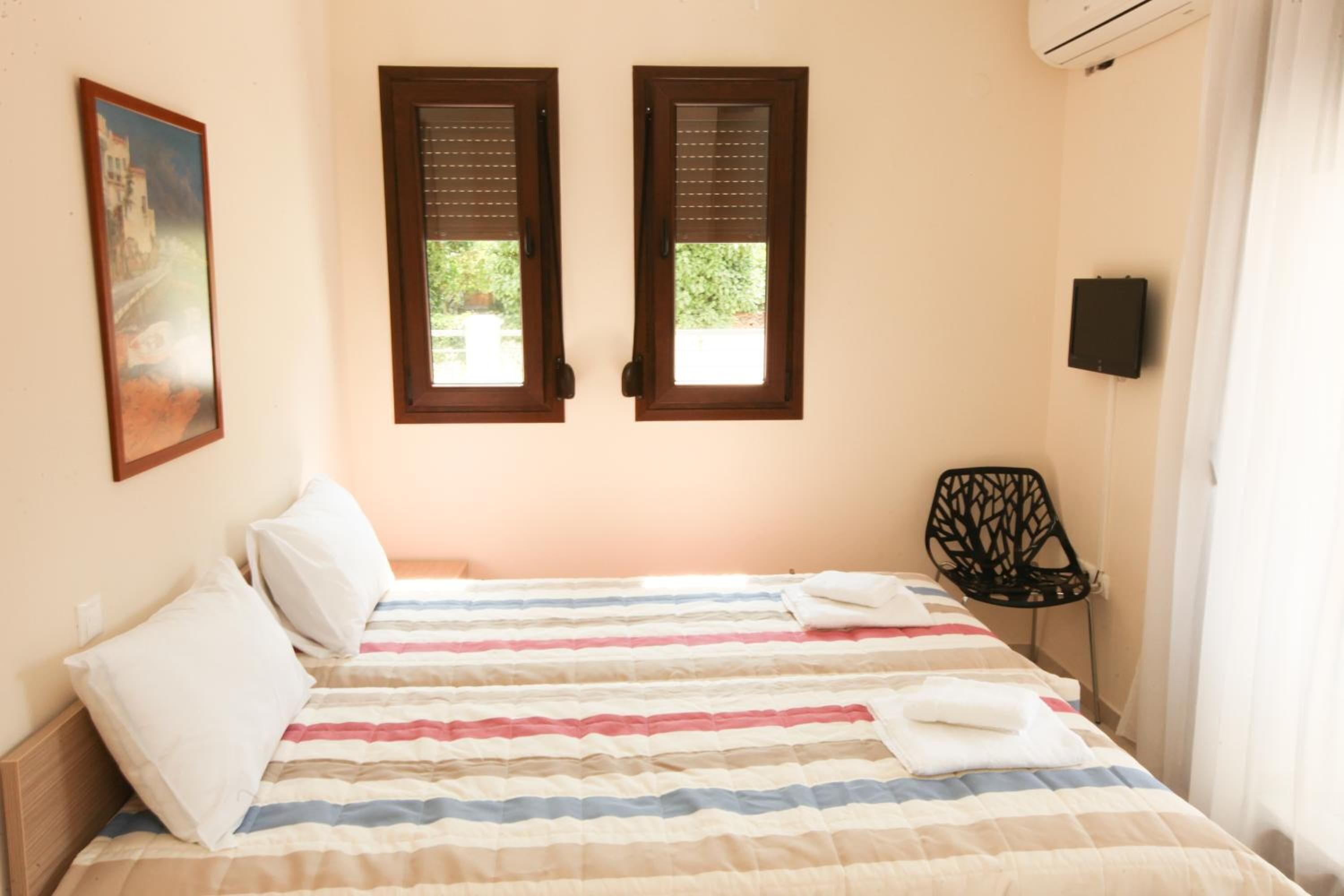 A bedroom with a bed, two windows, a chair, and a painting on the wall.
