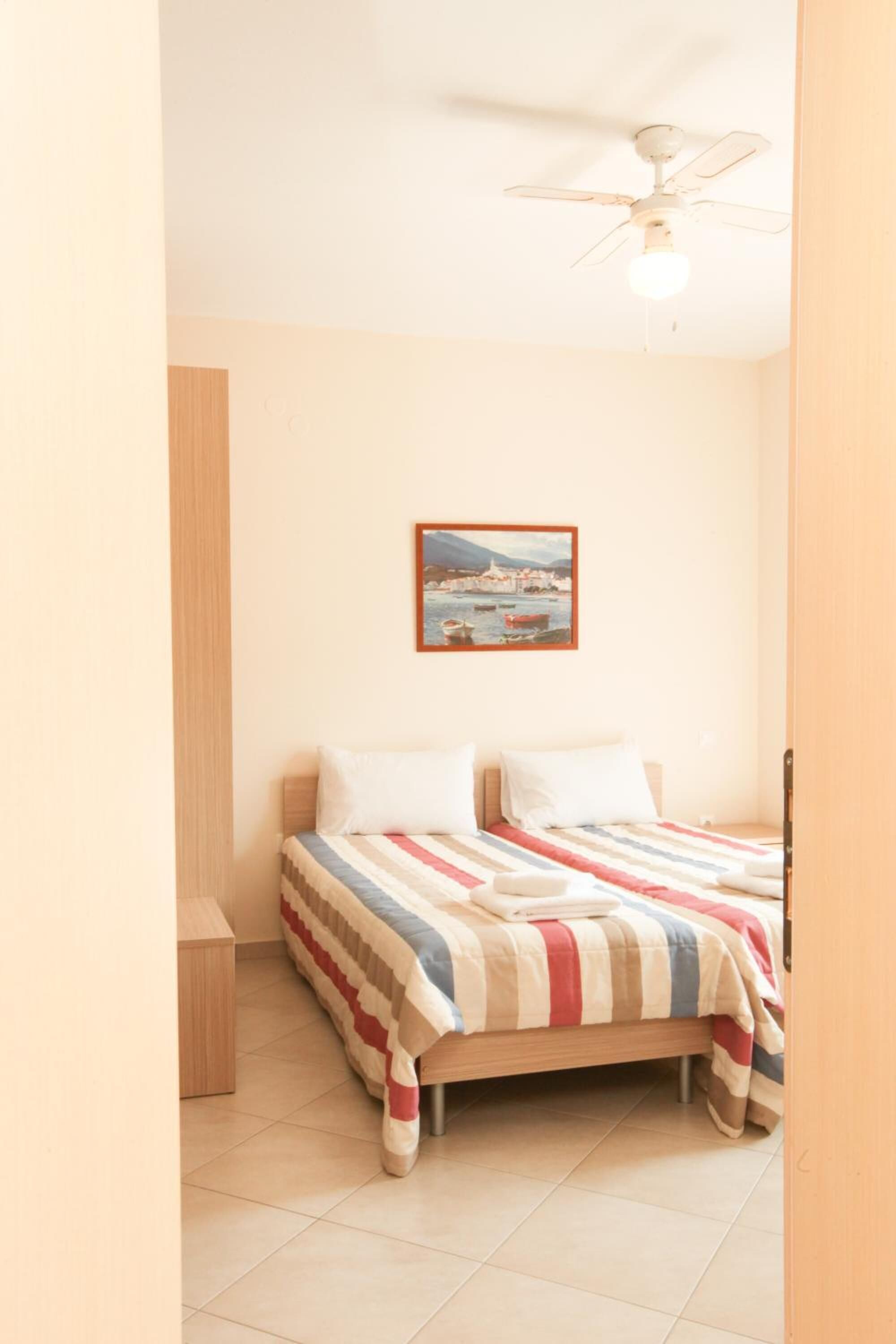 Un dormitorio con cama, ventilador de techo, mesita de noche y un cuadro en la pared.