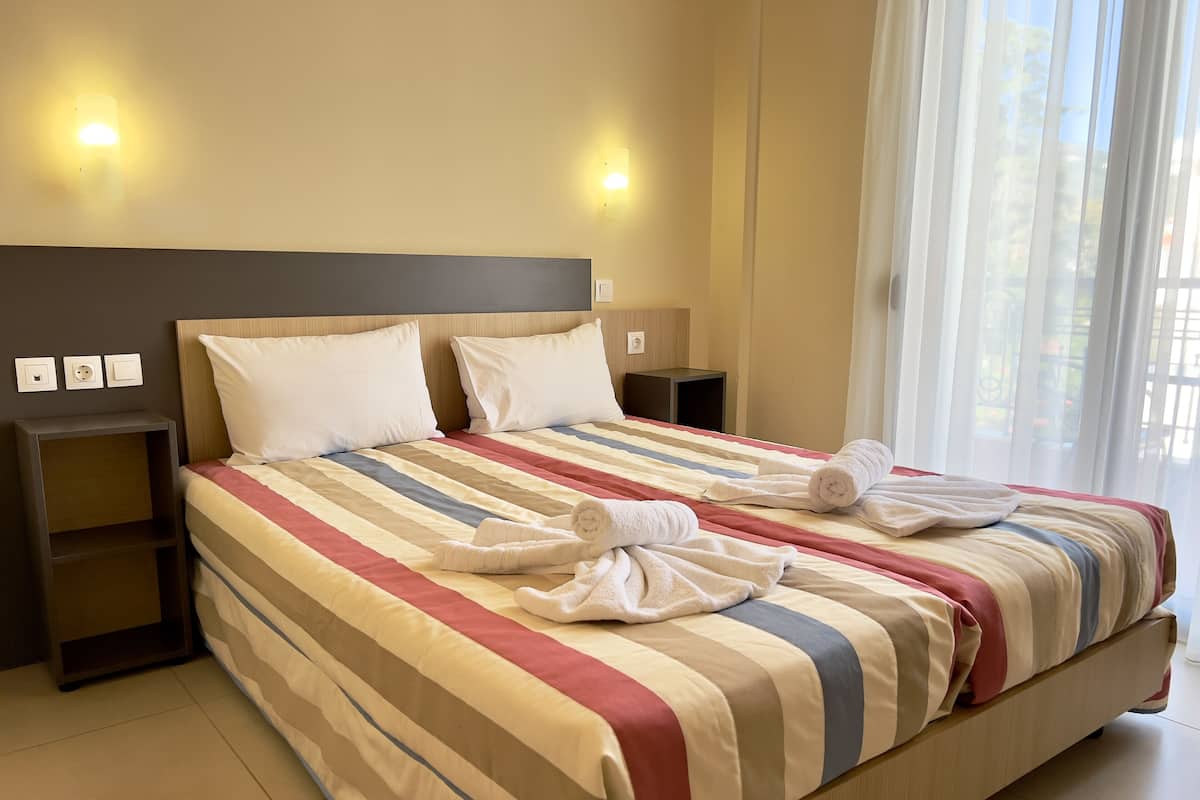 A neatly made bed with striped bedding and two pillows, a bedside table with a lamp, and a window with sheer curtains.