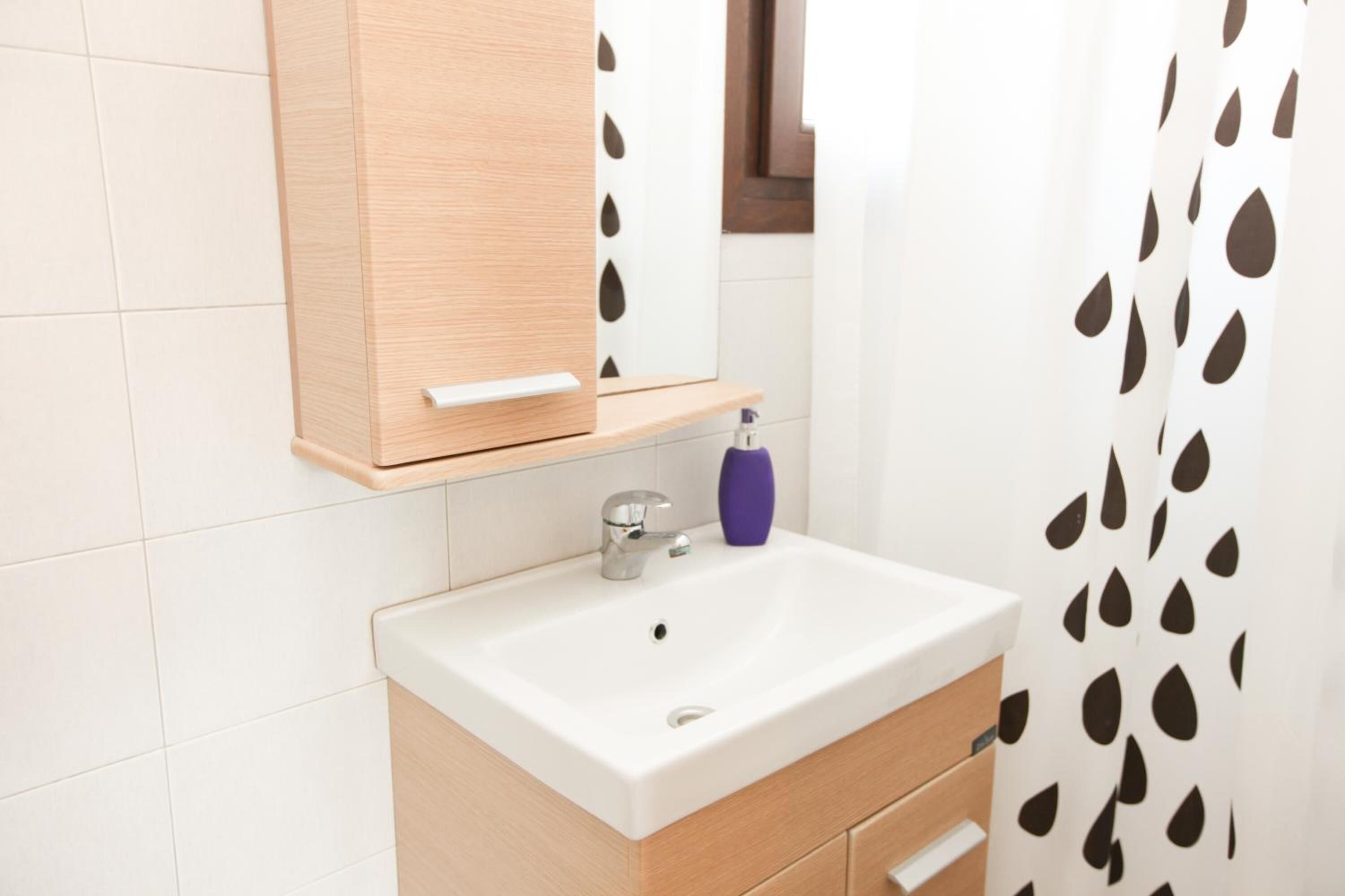 Un baño con un lavamanos blanco, tocador de madera y un espejo encima.